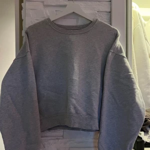 Grå croppad sweatshirt från BikBok - Säljer en grå croppad sweatshirt från BikBok med oversized passform och långa ärmar. Tröjan har en klassisk rund halsringning och är tillverkad i mjuk bomullsblandning, perfekt för chill dagar eller när du vill ha en enkel och stilren look.