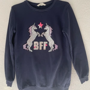 Mörkblå BFF-tröja med paljett-unicorns H&M - Mörkblå sweatshirt från H&M med glittriga paljett-unicorns och texten BFF framtill. Tröjan har rund hals, långa ärmar och är gjord i mjuk bomulls- och polyestermix. Perfekt för dig som älskar enhörningar och glitter!