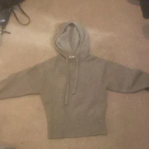 Grå stickad hoodie från Zara - Mysig grå stickad hoodie från Zara med huva och snörning. Tröjan har långa ärmar och bred ribbad mudd nedtill för en snygg passform. Använd max 2 gånger. 
