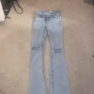 Håliga Bootcut jeans från Nelly  - Snygga ljusblå bootcut jeans från Nelly med slitna knän och broderade bakfickor i rosa. Jeansen har låg midja. Använt max 2 gånger. 
