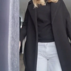 Svart lång kappa med klassisk krage - Säljer en svart kappa med klassisk krage och rak passform. Jackan är lång och har diskreta fickor på sidorna. Perfekt för dig som gillar stilrena och enkla plagg. Materialet känns mjukt och har en ull-liknande struktur. Passar dig som vill ha en tidlös look. Har katt så de kan vara lite katthår på den men det går att rolla bort