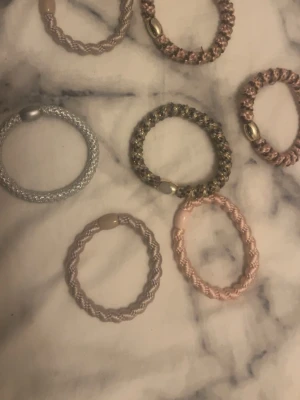 Set med spiralformade hårsnoddar - Säljer ett set med sju spiralformade hårsnoddar i olika färger som silver, rosa, beige och brons. Snoddarna har metalliska detaljer och är gjorda i elastiskt material med glansig finish. Perfekta för att skapa snygga frisyrer och hålla håret på plats.