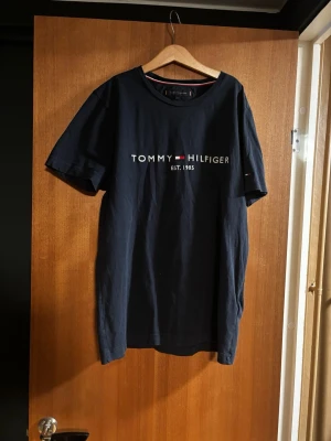 Marinblå Tommy Hilfiger t-shirt - Snygg marinblå t-shirt från Tommy Hilfiger med klassisk logga och texten 'EST. 1985' på bröstet. T-shirten har rund halsringning, korta ärmar och är gjord i mjuk bomull. Perfekt för en clean och stilren look.