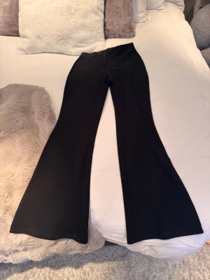 Svarta bootcut leggings från H&M - Säljer ett par svarta leggings med bootcut-modell. De har hög midja och är tillverkade i ett stretchigt material som sitter tight upptill och släpper ut nedtill för en snygg siluett. Perfekta för dig som gillar en trendig och bekväm look.
