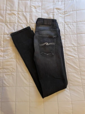 Mörkgrå nudie jeans - Säljer ett par mörkgrå nudie jeans som endast är använda ett fåtal gånger, skick 10/10!🔥Jeansen är W28 och L32 (kan vara lite längre i storleken så ca L33). Bara att höra av dig vid andra frågor👑