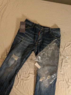 Dsquared2 jeans - Här har vi jeans från Dsquared2 med slitningar och trasiga detaljer på benen. Dome i ganska bra skick endå och kostar lite jämfört med andra, Jeansen har klassisk femficksmodell, knappgylf och coola slitningar för en trendig look. Perfekta för dig som gillar streetwear och vill sticka ut!