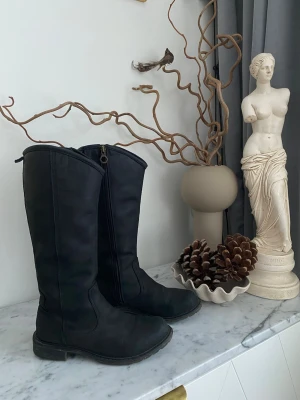 Svarta höga stövlar med dragkedja - Säljer ett par svarta höga boots från Timberland i damstorlek 38. Skorna är använda men fortfarande i mycket fint skick, med fint helhetsintryck och gott om liv kvar. Rejäla, bekväma och stabila – perfekta för vardag, promenader och kyligare dagar. Klassisk Timberland-design som håller säsong efter säsong.  Nypris: ca 2 000 kr Spana gärna på mina andra annonser så kan vi samfrakta.  (Sökord: Timberland boots dam stl 38 svarta höga skor)