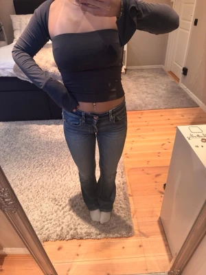 Mörkgrå offshoulder topp - Trendig mörkgrå offshoulder topp med långa ärmar och croppad passform. Toppen är åtsittande och har en stilren, enkel design utan synliga detaljer. Perfekt för dig som gillar minimalistisk stil.