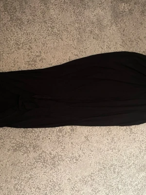 Svart långkjol i tunn polyester - Säljer en svart långkjol i tunn och luftig polyester. Kjolen har en enkel och rak design, perfekt för dig som gillar stilrena plagg. Materialet är lätt och faller snyggt längs benen. Passar till många olika looks!