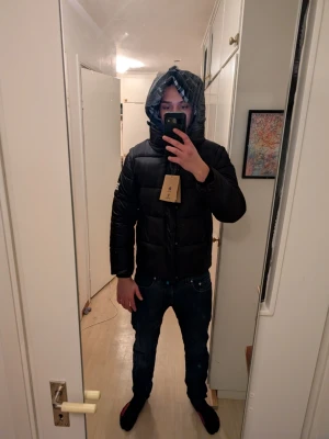 Svart dunjacka med huva från Burberry london - Säljer en svart dunjacka från Burberry med huva och dragkedja. Jackan kan bli till en väst och har storleken L