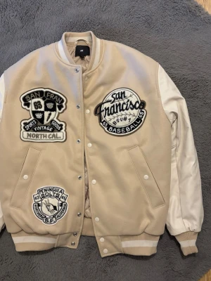 Beige bomberjacka med patches H&M - Aldrig använd - Snygg baseballjacka från H&M. Aldrig använd och nytvättad. Köpt på H&M för ca 800 kr för 2–3 år sedan.  Jackan är i väldigt fint skick och passar perfekt till en casual eller streetstyle-look. Skickas snabbt eller möts upp enligt överenskommelse. Skriv gärna vid frågor! 
