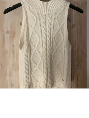Vit kabelstickad väst - Kabelstickad väst i mjuk vit ullmix med ribbad hög hals och breda ärmhål. Köpt på Lindex för nått år sen men aldrig använd och finns inte att köpa längre! Tveka inte att skriva vid frågor!🫰🏼🫰🏼