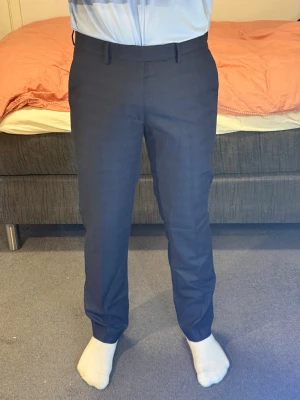 Mörkblå kostymbyxor med rak passform - Snygga mörkblå kostymbyxor med klassisk rak passform och bälteshällor. Byxorna har två fickor fram och två bakfickor med knappar. Perfekta till skjorta eller kavaj för en clean och stilren look.