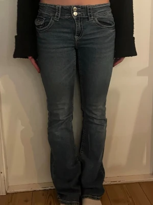 Blå bootcut jeans med dubbla knappar - Snygga blå bootcut jeans med dubbla silverfärgade knappar och klassiska fickor fram och bak. Jeansen har en lätt tvättad look och markerade sömmar. Perfekta för dig som gillar en tidlös och trendig stil. Från Gina tricot i storlek 170, ungefär S. Pris kan diskuteras!! 🙏🏻🩷