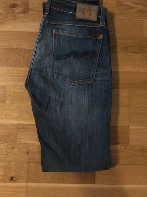 Blå jeans från Nudie Jeans - Säljer ett par klassiska blå jeans från Nudie Jeans med raka ben, orange sömmar. Perfekta för dig som gillar en avslappnad stil. Litet rivmärke och nypris ca 1600.