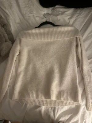 Offwhite stickad tröja Gina Tricot - Mysig offwhite stickad tröja från Gina Tricot med bred ribbad krage som kan bäras off shoulder. Tröjan har långa ärmar och ribbade muddar vid ärmslut och nederkant. Perfekt för kalla dagar och enkel att matcha med olika outfits.