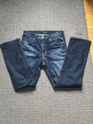 Blå Replay jeans straight fit - Snygga blå jeans från Replay med klassisk femficksdesign och raka ben. Jeansen har en mörk tvätt med subtila slitningar och detaljerade sömmar på bakfickorna. Tillverkade i slitstarkt denim för en tidlös look.