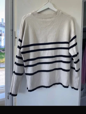 Randig beige stickad tröja - Säljer en beige stickad tröja med svarta ränder, tröjan har långa ärmar, ribbade muddar och en avslappnad passform. Materialet känns mjukt och bekvämt, perfekt för kyligare dagar. 💞Klassisk och enkel design som passar till det mesta. Säljer då den inte kommer till användning längre 😊