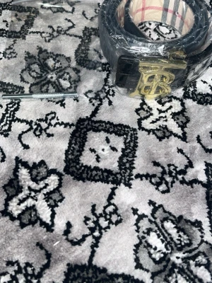 Svart Burberry bälte med guldspänne 110cm  - Snyggt svart bälte från Burberry med klassiskt rutmönster och ett stort guldigt BB-spänne framtill. Insidan har det ikoniska Burberry-mönstret i beige, rött och svart. Perfekt accessoar för att lyfta din outfit. 