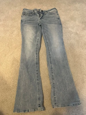 Ljusblå bootcut jeans från True Religion - Snygga ljusblå bootcut jeans från Ture Religion med klassisk femficksdesign och normal midja. Jeansen har en lätt tvättad look och är tillverkade i mjukt bomullsmaterial. Perfekta för dig som gillar en avslappnad men trendig stil. Aldrig använda 