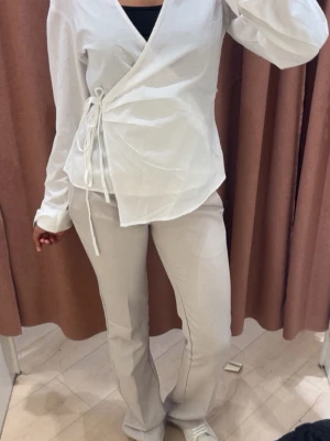 Vit omlottblus med snörning - Snygg vit omlottblus med snörning i sidan och v-ringad hals. Långärmad modell i lätt och luftig bomull, perfekt för en trendig och stilren look. Passar dig som gillar en modern och avslappnad stil. Knappt använd 