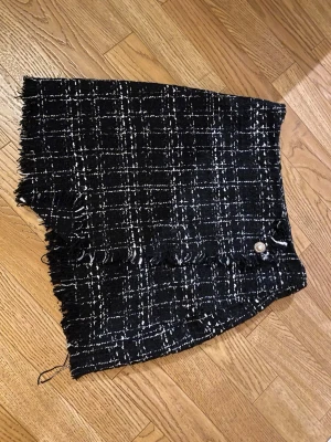 Svart rutig kortkjol från Shein - Säljer en svart och vit rutig kortkjol från Shein i storlek XS. Kjolen har fransiga kanter, dekorativ knapp framtill och ett snyggt rutmönster. Perfekt för dig som gillar trendiga detaljer och vill sticka ut lite extra.