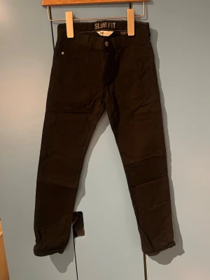 Svarta slim fit jeans - Svarta slim fit jeans med klassisk femficksdesign och knappgylf. Jeansen har en smal passform och är tillverkade i ett stretchigt material som ger en bekväm känsla. Perfekta för dig som gillar en stilren och enkel look.