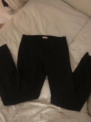 Svarta kostymbyxor från Nelly - Stilrena svarta kostymbyxor från Nelly med klassisk rak passform och låg midja. Byxorna har en enkel design utan synliga detaljer och passar perfekt till en dressad look. I storlek 38. 