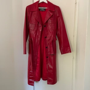 Röd skinn trenchcoat - Säljer en unik vintage skinnrock i äkta skinn. Den är köpt i Rumänien, den är cirka 24 år gammal men fortfarande i mycket fint skick. Modellen är tidlös och har en riktigt snygg röd färg som gör att den sticker ut, passar perfekt för dig som vill stå ut. Den är i storlek Xxl men är liten i storlek så det passar dig som har   s/m. Den säljs inte längre på nätet, har använt ca 2-3 gånger men den passar inte mig längre. Skicka gärna ett meddelande för bild på.💕