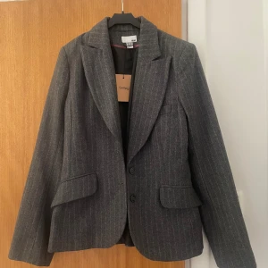 Kavaj  - Säljer denna fina gråa figurformade kavajen med diskreta ljusrosa ränder. Den är nyligen inköpt från Sellpy men passade tyvärr inte mig i storleken!