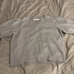 Grå stickad tröja från ONLY - Mysig grå stickad tröja från ONLY i storlek M. Tröjan har puffade axlar och ribbade muddar vid hals, ärmslut och nederkant. Enkel och clean design som funkar till jeans eller kjol. Perfekt för kyliga dagar och sköna hemmakvällar.