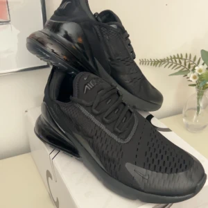 Nike Air Max 270 helsvarta sneakers - Säljer ett par helsvarta Nike Air Max 270 sneakers med snygg, sportig design. Skorna har en luftig mesh-ovandel, synlig Air Max-dämpning i hälen och klassisk snörning. Perfekta för dig som gillar stilrena och bekväma sneakers med modern känsla.