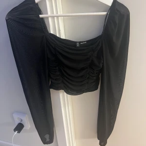 Svart mesh topp med rynkade detaljer - Trendig svart topp från H&M med långa meshärmar och rynkade detaljer framtill. Toppen har en croppad passform och fyrkantig urringning som ger en snygg siluett. Perfekt för dig som vill sticka ut med en cool och modern look.