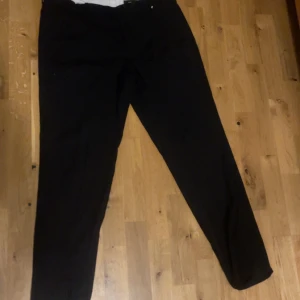 Svarta kostymbyxor från H&M - Svarta kostymbyxor från H&M i klassisk rak modell. Byxorna har normal passform och är perfekta för en clean och stilren look. Tillverkade i ett mjukt material som känns bekvämt hela dagen. Passar dig som gillar enkel och tidlös stil.