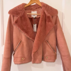 Rosa pälsig jacka, OANVÄND - Säljer en snygg rosa aviator jacka från River Island, i storlek 36. Helt ny o köpt för 700kr. Säljer för mindre än hälften. Jackan har fluffig päls krage, croppad passform och är helt i rosa. Materialet är mjukt och känns lyxigt med fluffig päls på hela insidan. 