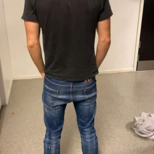 Blå dsquared jeans med färgstänk - Säljer ett par blå dsquared jeans med coola färgstänk och slitningar på benen. Jeansen har en normal passform, klassiska fem fickor och låg midja. Materialet är robust denim och de har en snygg tvättad look som ger dem extra edge.