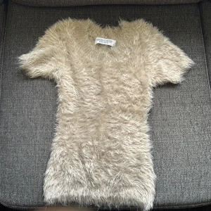 Beige fluffig topp Chiara Forthi storlek xs - Supermjuk och fluffig beige topp från Chiara Forthi Milano. Kortärmad med v-ringning och en liten guldfärgad detalj bak i nacken.