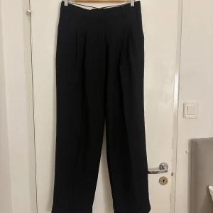 Svarta kostymbyxor  - Säljer mina super snygga kostymbyxor som är super sköna att ha. De kommer tyvärr inte till användning längre då det inte passar mig! Man kan båda ha byxorna som et är eller så kan man vika in satt den vita sidan syns utåt vilket är väldigt snyggt. Super bra skick! Går hela vägen ner på mig som är 168cm ungefär. Knappen kan behövas sys om! Hund finns i hemmet! se stl på bild!🩷