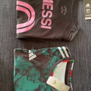 Adidas Messi fotbollströja svart/rosa och Italien tröja  - Snygg svart fotbollströja från Adidas med Messi-tryck i rosa och texten 'Freedom to Dream' på bröstet. Tröjan har korta ärmar och är tillverkad i ett lätt, tekniskt material som andas. Perfekt för dig som vill sticka ut på planen.