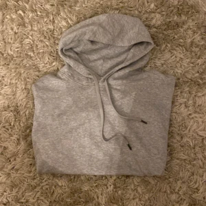 Grå hoodie från Stone Island - Snygg grå hoodie från Stone Island med klassisk patch på ärmen. Tröjan har huva med snörning, känguruficka och ribbade muddar. Tillverkad i mjuk bomull, perfekt för chill dagar. Enkelt och stilrent plagg som funkar året runt.