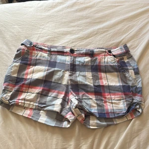 Rutiga shorts från Cubus, stl 40 - Säljer ett par rutiga shorts från Cubus i storlek 40. De har en mix av blått, vitt, grått och rosa i mönstret, klassisk passform med knappar och fickor både fram och bak. 