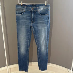 Blå jeans från Nudie Jeans - Snygga blå jeans från Nudie Jeans med klassisk femficksdesign och kontrastsömmar. Jeansen fått en tvär fet tvätt genom användning de är storlek W31 L30 modellen heter Lean Dean 