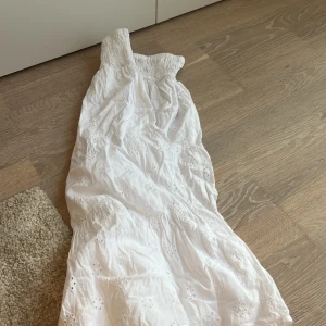 Vit långkok från Gina Tricot - Supersöt vit långkjol från Gina Tricot med smock upptill och broderade blommor över hela klänningen. Klänningen är ärmlös och har en luftig känsla, perfekt för varma dagar. Tillverkad i bomull för extra komfort.