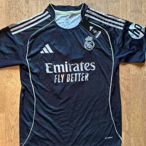 Real Madrid Valverde #8 marinblå tröja - Snygg Real Madrid fotbollströja från Adidas i marinblått med vita detaljer och broderat klubbmärke. Nummer 8 och Valverde på ryggen, samt klassiska Adidas-ränder på axlarna. Tillverkad i lätt och ventilerande Aeroready-material, perfekt för match eller träning. Skriv privat för mer frågor 