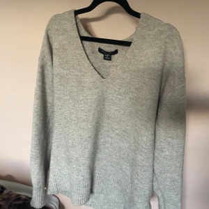 Grå stickad v-ringad tröja Amisu - Mysig grå stickad tröja från Amisu med djup v-ringning och långa ärmar. Tröjan har en relaxed fit och ribbade muddar vid ärmslut och nederkant. Perfekt för lager-på-lager under kyliga dagar. Super najs nu i höst 🍂🥃🪐