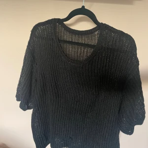 Svart stickad tröja med kort ärm - Säljer en svart stickad tröja med grovstickat mönster och korta ärmar. Tröjan har en avslappnad passform och rund halsringning, perfekt att slänga på sig över ett linne eller t-shirt. Enkel och stilren design som funkar till många outfits. Jättelätt att styla och super snygg💘💘.står inte vilken storlek men skulle säga L