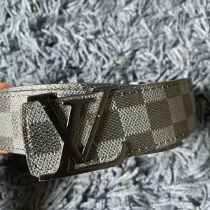 rutigt skärp i läder - Snyggt bälte med klassiskt rutigt mönster i svart och grått. Bältet har en stor logga i metall som spänne och är gjort i skinn. Perfekt accessoar för att lyfta din outfit med en lyxig touch.
