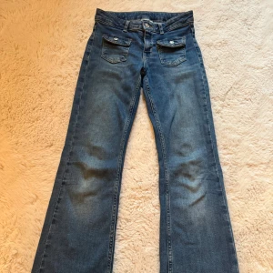 Blå bootcut jeans från Kappahl - Snygga blå jeans från Kappahl i storlek 152. Modellen har bootcut-ben, klassiska fem fickor och coola detaljer med knappar på framfickorna. Jeansen är tillverkade i denim och har normal passform med medelhög midja. Köpte för 369 och säljer för mkt billigare plus ingen frakt!