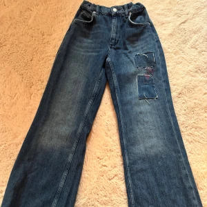Blå wide jeans från Zara med patch - Snygga blå jeans från Zara i modell med breda ben och hög midja. Jeansen har coola patch-detaljer på ena benet och klassisk femficksdesign. Tillverkade i jeansmaterial med elastisk midja bak för extra komfort. Väldigt bagy! Säljer för väldigt bra pris och ingen frakt!