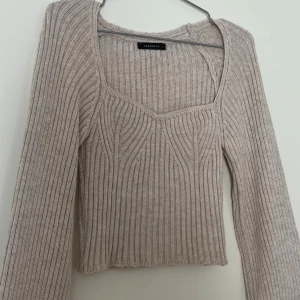 Beige ribbad stickad tröja Trendyol - Snygg beige stickad tröja från Trendyol med ribbad struktur och långärmad design. Tröjan har en feminin, något croppad passform och en unik halsringning som ger en cool touch. Perfekt att styla med jeans eller kjol för en trendig look.